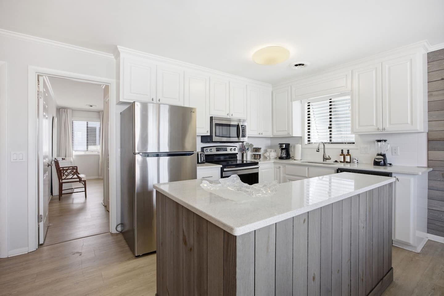 A modern kitchen with white cabinetry, a stainless steel refrigerator, a microwave, and a wooden island.