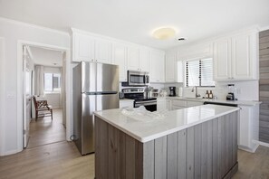 A modern kitchen with white cabinetry, a stainless steel refrigerator, a microwave, and a wooden island. - 2BD, 2BA duplex just 470 ft from beach access at Wrightsville Beach! (Wrightsville Beach)