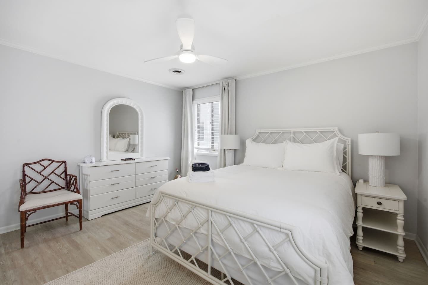 A bedroom with a bed, a dresser, a chair, a mirror, a window with curtains, and a ceiling fan.