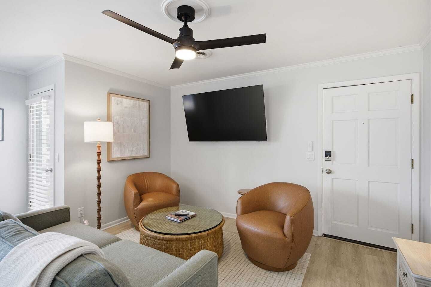 A living room with a ceiling fan, a flat-screen TV, two leather armchairs, a round coffee table, and a sofa.