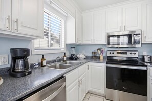 A modern kitchen with white cabinets, a built-in microwave, a stainless steel oven, a coffee maker, and a dishwasher. - This apartment is a 2 bedroom(s), 2 bathrooms, located in Wrightsville Beach, NC. (Wrightsville Beach)