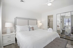A bedroom with a bed, bedside lamps, a nightstand, a mirror, and a closet. - This apartment is a 2 bedroom(s), 2 bathrooms, located in Wrightsville Beach, NC. (Wrightsville Beach)
