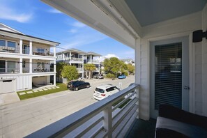 A balcony with a view of a street, a building with multiple balconies, and a door with a black handle. - This apartment is a 2 bedroom(s), 2 bathrooms, located in Wrightsville Beach, NC. (Wrightsville Beach)