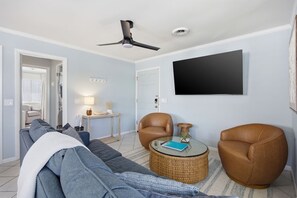 A living room with a sofa, two leather chairs, a round coffee table, a ceiling fan, a flat-screen TV, and a small side table. - This apartment is a 2 bedroom(s), 2 bathrooms, located in Wrightsville Beach, NC. (Wrightsville Beach)