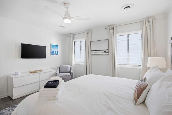 A hotel room with a bed, a desk, a chair, a TV, and a window with curtains. - This apartment is a 2 bedroom(s), 2 bathrooms, located in Wrightsville Beach, NC. (Wrightsville Beach)