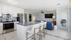 A modern kitchen with white cabinets, stainless steel appliances, and a bar area with stools. - Coastal 4BR/4BA coastal duplex featuring king and queen ensuite bedrooms, a fully stocked kitchen, fenced pet-friendly yard, outdoor shower, beach gear, Smart TVs, WiFi, and parking for up to 6+ vehicles. (Wrightsville Beach)