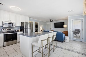 A modern kitchen with white cabinets, stainless steel appliances, and a bar area with stools. - Coastal 4BR/4BA coastal duplex featuring king and queen ensuite bedrooms, a fully stocked kitchen, fenced pet-friendly yard, outdoor shower, beach gear, Smart TVs, WiFi, and parking for up to 6+ vehicles. (Wrightsville Beach)