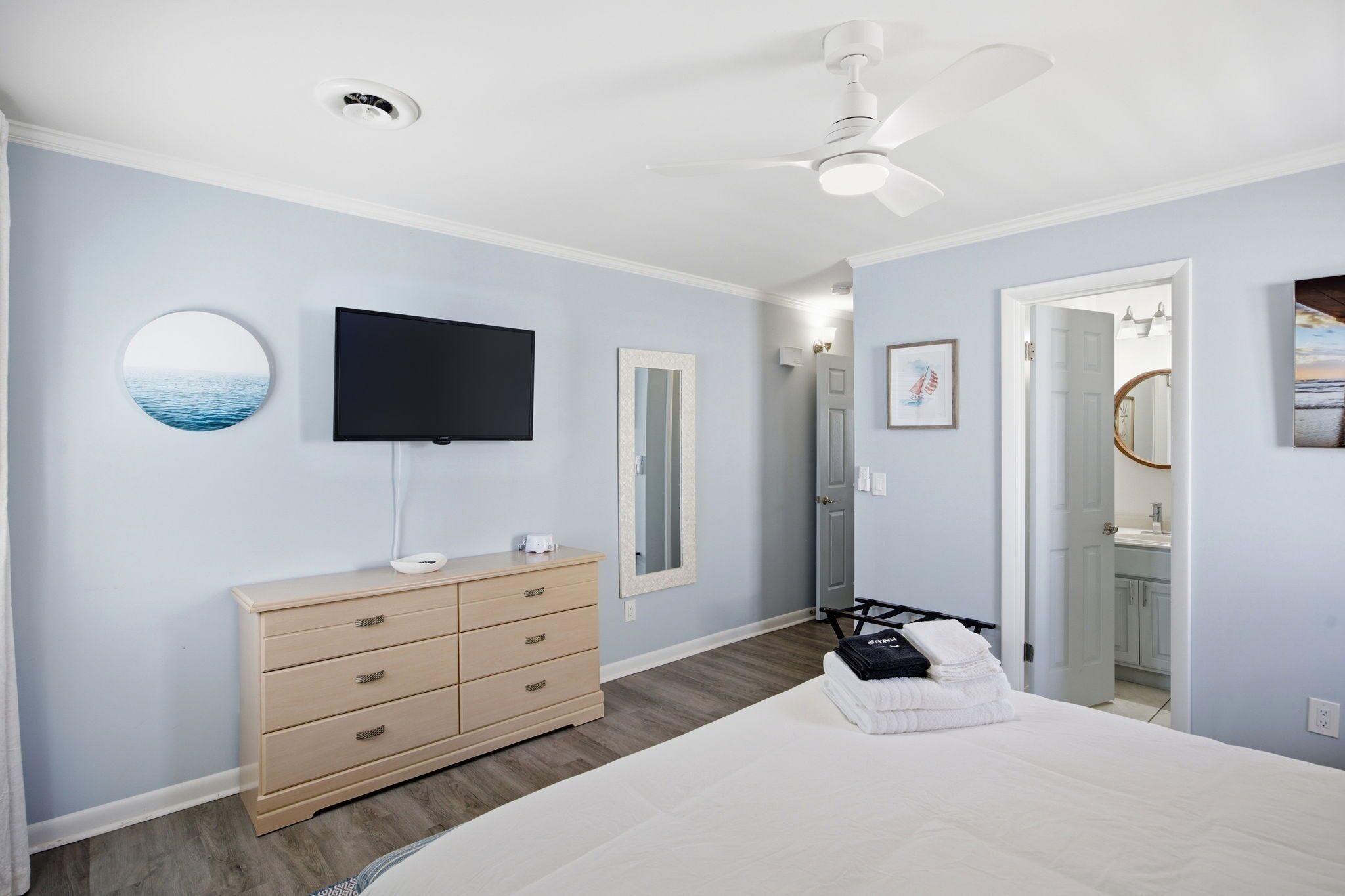 Un dormitorio con cama, cómoda, televisor, ventilador de techo y puerta de baño.