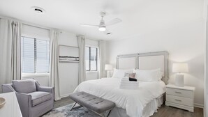 A bedroom with a bed, bedside tables, a bench, a chair, and a ceiling fan. - Coastal 4BR/4BA coastal duplex featuring king and queen ensuite bedrooms, a fully stocked kitchen, fenced pet-friendly yard, outdoor shower, beach gear, Smart TVs, WiFi, and parking for up to 6+ vehicles. (Wrightsville Beach)