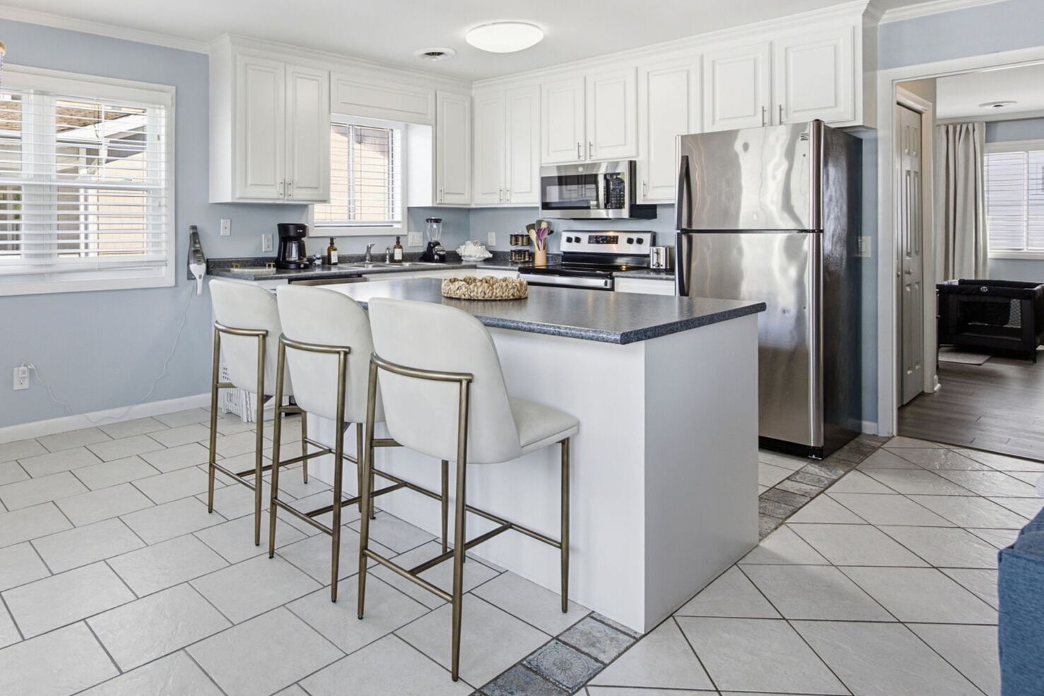 A modern kitchen with white cabinets, a stainless steel refrigerator, and a central island with bar stools.