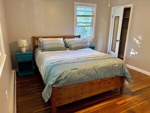 Ein Schlafzimmer mit einem hölzernen Bett, einem Nachttisch mit Lampe, einem Fenster mit Jalousien und einer Tür zu einem Kleiderschrank.