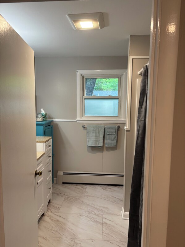 A bathroom with a window, a towel rack, a towel, a heater, and a door. - Centrally located 3-bedroom house in quiet neighborhood. (Ellsworth)