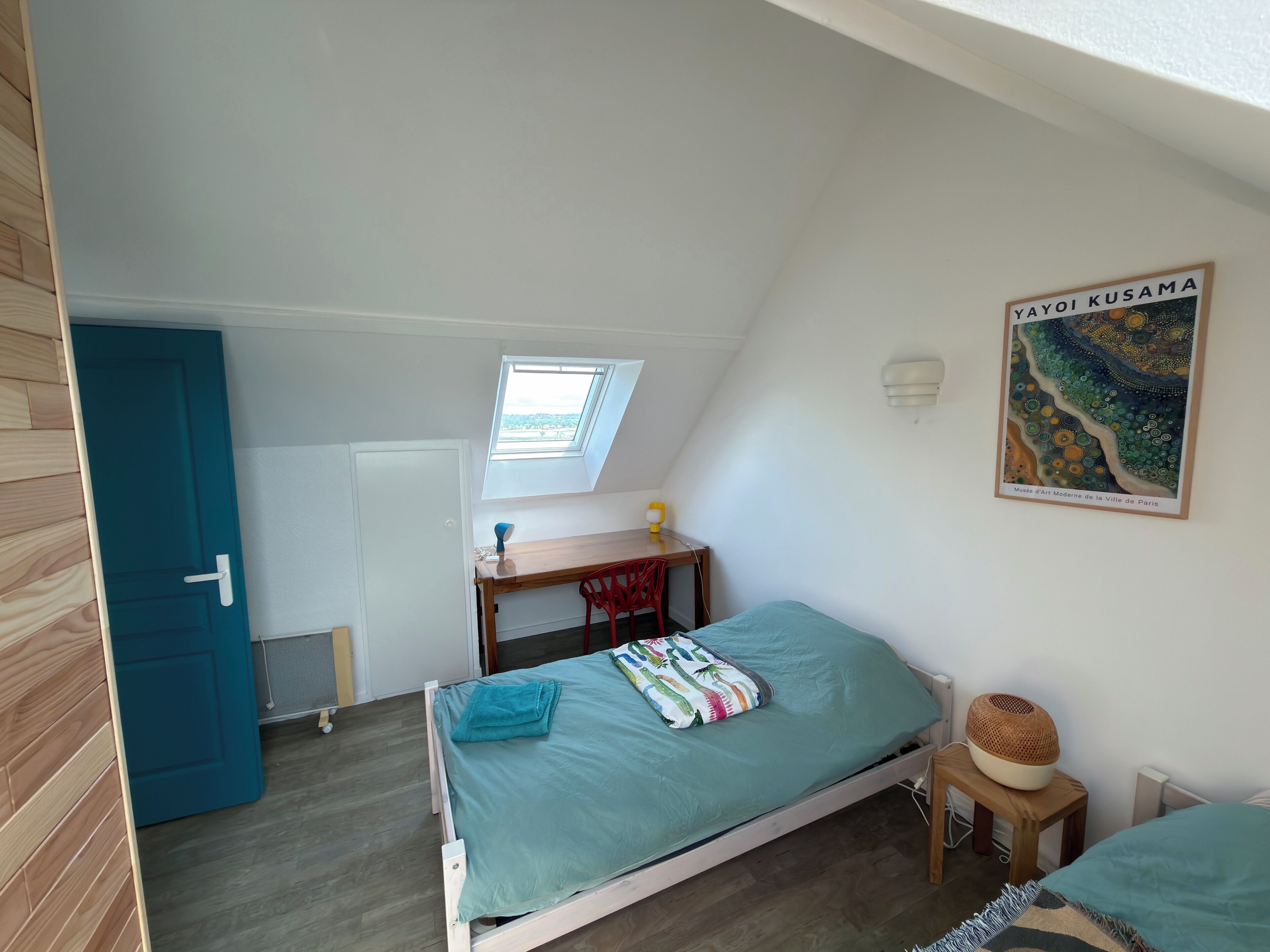 A bedroom with a bed, a desk, a chair, a window, and a wall-mounted light fixture.