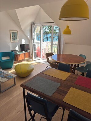 Una sala de estar moderna con una mesa de comedor de madera, sillas azules y amarillas, una lámpara colgante amarilla y un televisor sobre un mueble de madera.