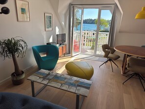 A modern living room with a large window, a television, a dining table, and a potted plant. - Apartment with terrace, sea view, direct beach access. Fiber. Refurbished. GR34. (Fouesnant)