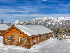 Eine Blockhütte mit schneebedecktem Dach, umgeben von schneebedeckten Bergen und Bäumen.