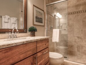 A bathroom with a marble countertop, wooden cabinetry, a glass shower enclosure, and a framed picture on the wall. - New to VRBO - Cowboy Heaven Cabin, Yellowstone Country, Hot Tub, Amazing Views! (Big Sky)