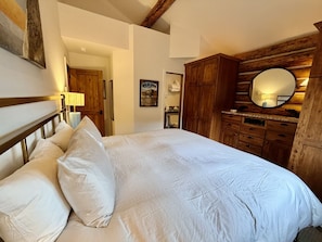 Quarto com cama grande, guarda-roupa de madeira e espelho.
