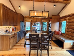 A kitchen with wooden cabinets, a granite countertop, a dining table with chairs, and a hanging light fixture. - New to VRBO - Cowboy Heaven Cabin, Yellowstone Country, Hot Tub, Amazing Views! (Big Sky)