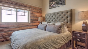 Quarto com uma cama grande, janela, cabeceira, mesa de cabeceira e um quadro na parede.