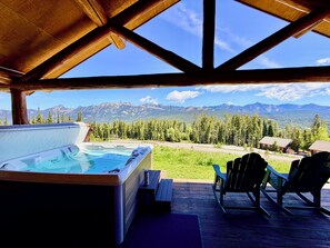 Un bain à remous sur une terrasse en bois, avec des chaises, offrant une vue sur un paysage montagneux.