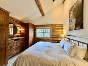 Een slaapkamer met een groot bed, een houten garderobe en een raam met uitzicht.