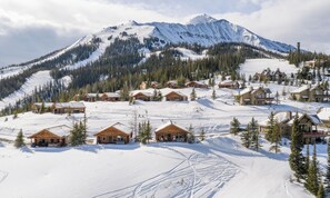 Montanha coberta de neve com estação de esqui, apresentando chalés de madeira e um grande hotel.