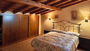 Une chambre à coucher avec un plafond en bois, un lit recouvert d’une literie à motifs floraux, deux lampes de chevet et une armoire.