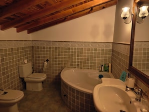 Une salle de bain équipée de toilettes, d’une baignoire et d’un lavabo, avec des poutres en bois au plafond et des murs recouverts de carreaux décoratifs.