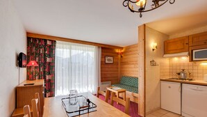 Habitación compacta con mesa de comedor, sillas, sofá, kitchenette y ventana con cortinas.