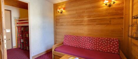 A wooden room with a bench, a table with a book, and a wall with two wall-mounted lights.