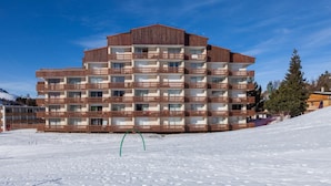 Un hotel de varios pisos con balcones, una pista de esquí al fondo y cielo despejado.