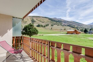 En balkon med gelænder af træ, en rød stol og udsigt over et grønt marklandskab og bakker.
