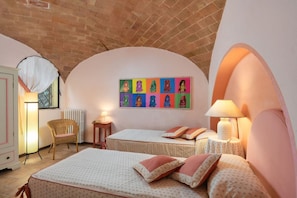 Ein Schlafzimmer mit zwei Betten, einem Korbstuhl, einer Heizung und einem farbenfrohen Kunstwerk an der Wand.