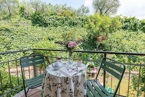 Ein Balkon mit Tisch für zwei Personen, einer Blumenvase und einem Buch.