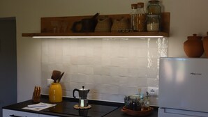 A kitchen with a black countertop, a white refrigerator, and a shelf with jars and a coffee pot.