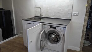 A compact kitchen with a built-in washing machine, a sink, and a black refrigerator.