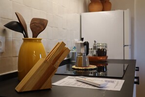 Una encimera de cocina con un jarrón amarillo, utensilios de madera, una cafetera y un refrigerador al fondo.