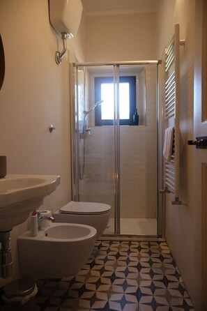 Un baño con ducha, inodoro, lavamanos y azulejos de suelo estampados.