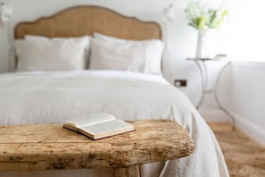 A neatly made bed with white bedding and pillows, an open book on a wooden table, and a bedside lamp. - Escape to a luxury 2 bdrm country cottage and ocean views (Kirkcaldy)