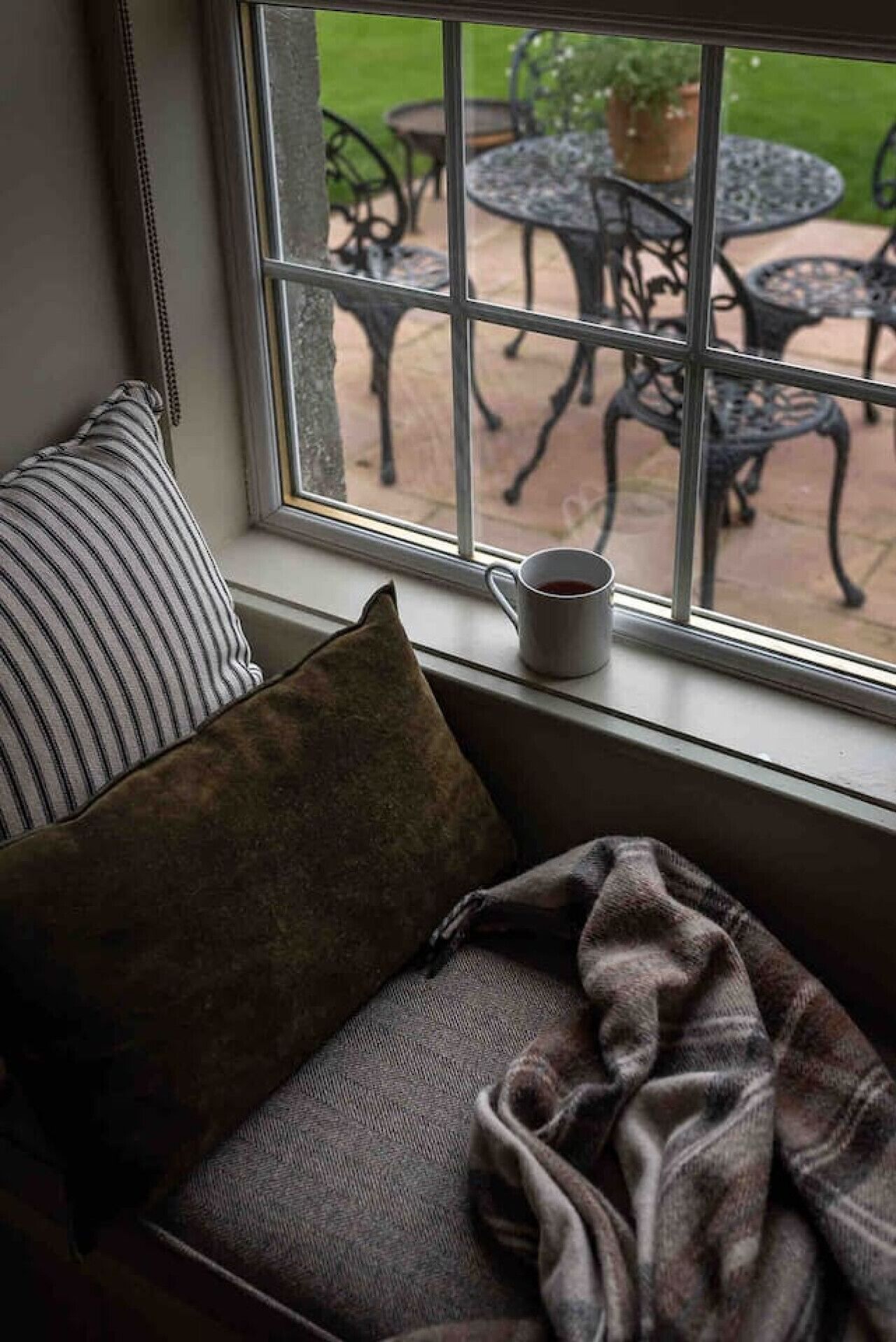A window seat with a cushion, a mug, and a view of outdoor patio furniture.