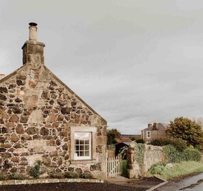 A stone cottage with a chimney, a small window, and a wooden gate. - Escape to a luxury 2 bdrm country cottage and ocean views (Kirkcaldy)