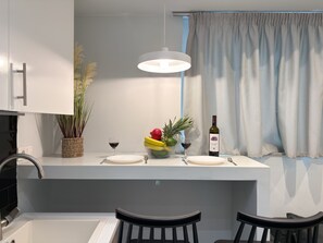 Une cuisine moderne avec un plan de travail blanc, un luminaire suspendu, une fenêtre avec des rideaux et un coin bar avec des tabourets.