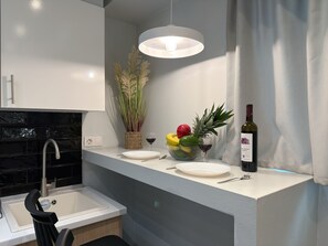 A modern kitchen with a white countertop, a built-in sink, a hanging pendant light, and a vase with dried plants. - SmartLiving Central Apt 2 (Thessaloniki)