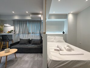 Une chambre d’hôtel moderne équipée d’un canapé, d’une table à manger, d’un lit avec des serviettes et d’un appareil de climatisation.