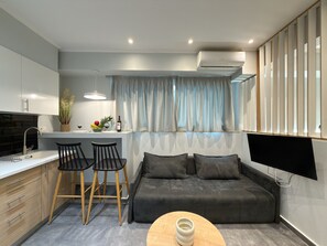 Un espace de vie compact comprenant un coin cuisine, un coin repas avec deux chaises, un canapé et un téléviseur à écran plat fixé au mur.