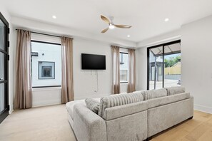 A modern living room with a sofa, a ceiling fan, a flat-screen TV, and large windows with curtains. - Newly Built Custom Luxury Home Rooftop Deck Midtown ATL (Atlanta)