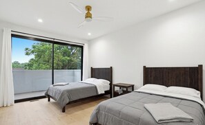 A bedroom with two beds, a ceiling fan, a window with a view of trees, and a small bedside table. - Newly Built Custom Luxury Home Rooftop Deck Midtown ATL (Atlanta)