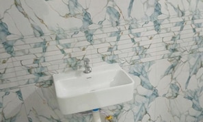 Un baño con lavamanos blanco, paredes con diseño de mármol y una tubería visible.