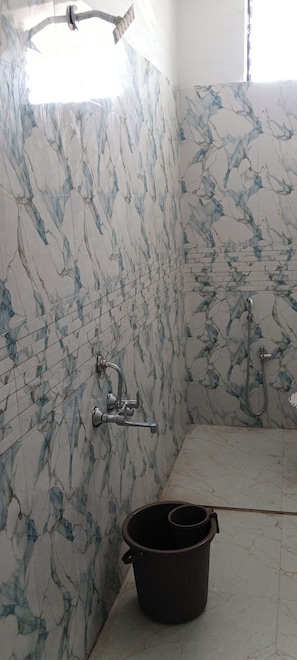 A bathroom with marble walls, a shower, and a bucket on the floor. - Hotel New Vivaantaa  (Chhatrapati Sambhajinagar)